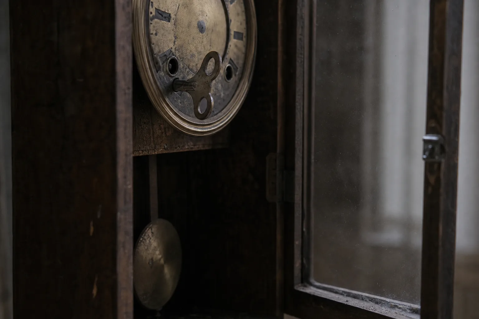 An old wall clock with its glass door open, a metal winding key set into the worn brass face.